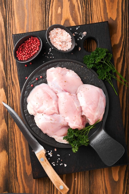 Raw chicken thigh fillet without skin with herbs and spices on old wooden background Farm poultry meat Top view with copy space Mock up