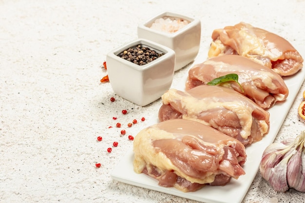 Raw chicken thigh without bones or skin. A useful ingredient for preparing healthy food, spices, garlic. Light putty background, copy space