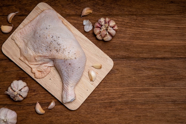 木製のテーブルに生の鶏もも肉とにんにく胡椒