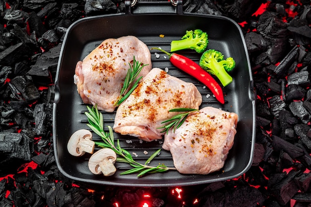 Raw chicken thighs in a pan stand on a hot barbecue grill