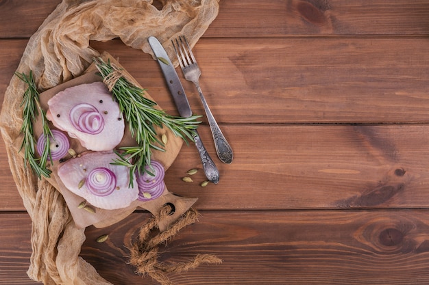 Raw chicken thighs with rosemary, red onion and peppercorns on cutting board. Uncooked poultry meat. Culinary cooking ingredients. Top view with copy space for text