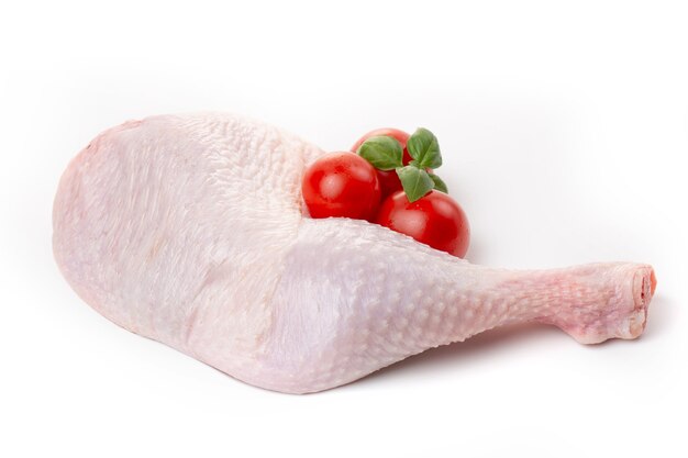 Raw chicken thighs with skin decorated with tomatoes and basil on a white background.