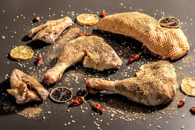 Raw chicken thighs with spices. A useful ingredient for preparing healthy food. Black stone background, trendy hard light, dark shadow, flat lay