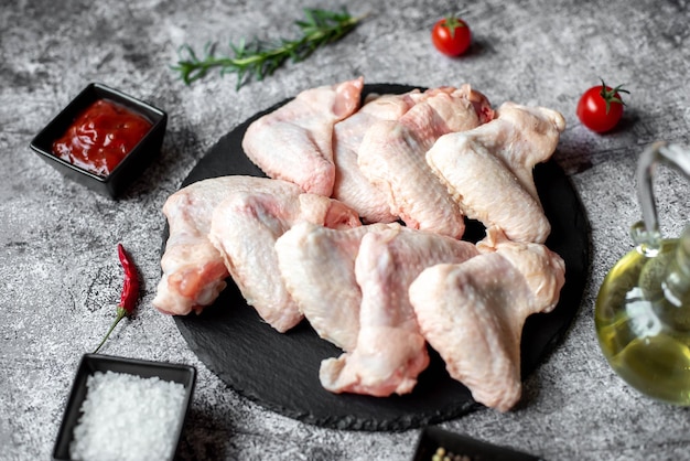 Raw chicken wings on a black plate with tomato sauce and a small bowl of tomato sauce.