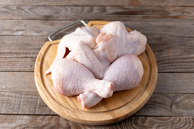 Raw chicken wings and drumsticks on cutting board on wooden table close-up.