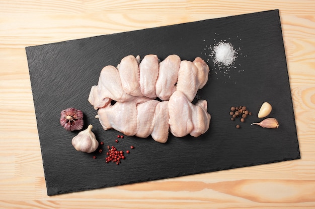 Photo raw chicken wings. fresh chicken wings with spices on cutting board. raw chicken wings with ingredients for cooking on a slate cutting board over wooden table.