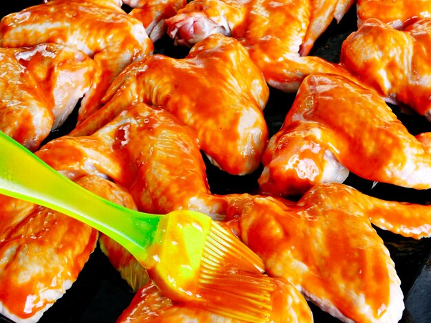 Сырые куриные крылышки в остром красном соусе на противне перед выпечкой.