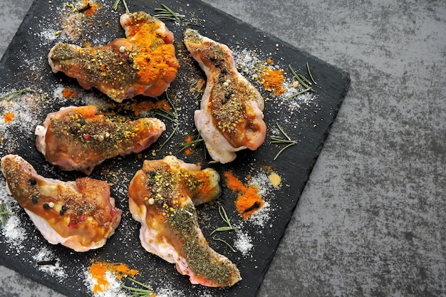 Ali di pollo crude marinate in spezie su un bordo di pietra nero.