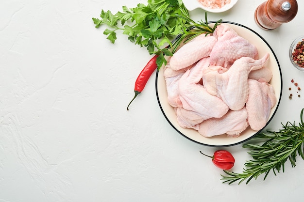 raw chicken wings in a white bowl with spices and ingredients for cooking 