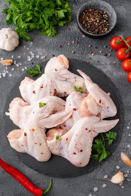 Raw chicken wings with fresh herbs spices for cooking on a dark concrete background Top view