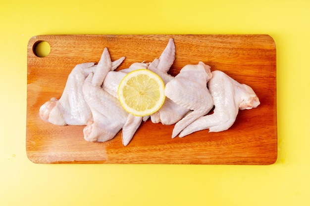 Raw chicken wings with lemon slices on cutting board isolated on yellow background Top view