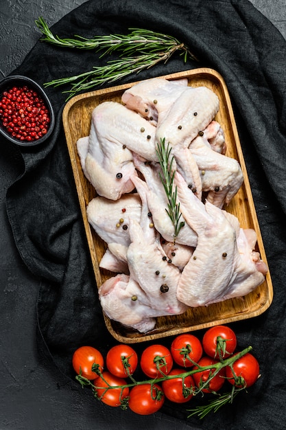 Foto ali di pollo crude in una ciotola di legno, cottura del rosmarino e del pepe rosa degli ingredienti, carne organica dell'azienda agricola, vista superiore.