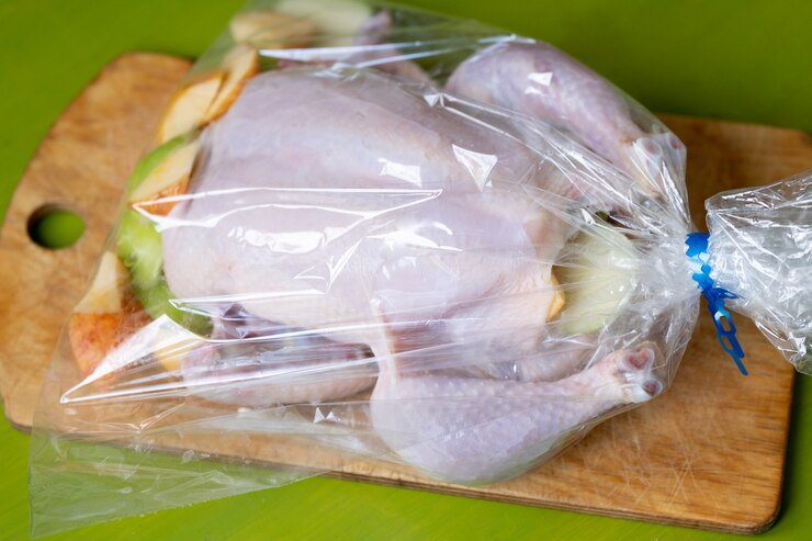 緑の背景の木製まな板の上に横たわっているプラスチックオーブンバッグにリンゴと生の鶏肉。健康的な食事の作り方