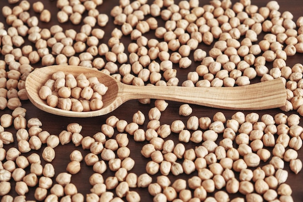 Raw chickpeas in a wooden spoon scattered on a wooden background