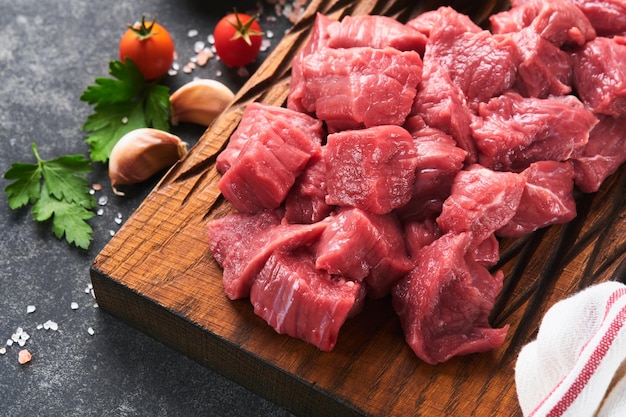 Raw chopped beef meat Raw organic meat beef or lamb spices herbs on old wooden board on dark grey concrete background Goulash Raw uncooked meat Meat with blood Top view with copy space