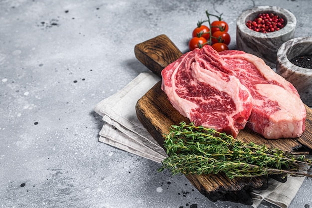 Raw Chuck Roll beef meat steaks on a wooden board with thyme. Gray background. Top view. Copy space.