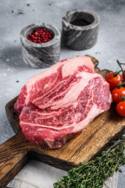 Raw Chuck Roll beef meat steaks on a wooden board with thyme Gray background Top view