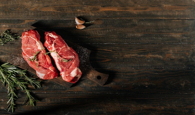 Raw chuck roll beef steaks on wooden background with rosemary and thyme