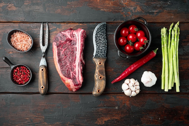 Raw club steak with ingredients on old dark wooden table