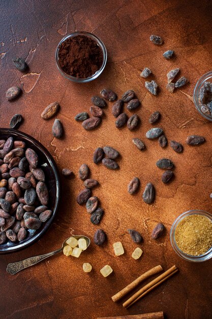 Фото Сырые какао-бобы, какао-порошок и коричневый сахар на темном каменном фоне, вид сверху, выборочное пространство для фокусировки текста