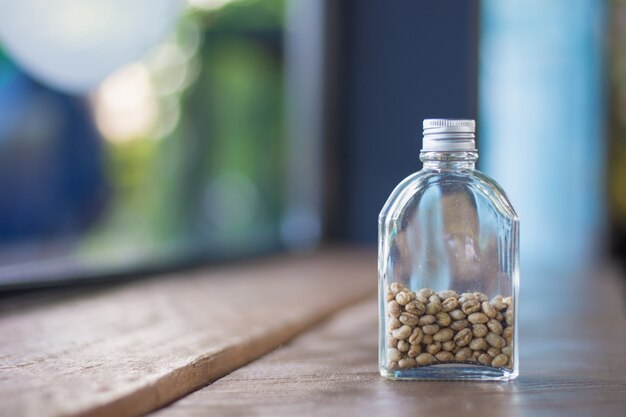 Raw coffee beans in bottles on a wooden table with indoor lighting background