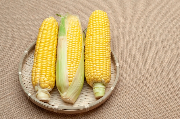 Raw corn cobs in a woven bamboo basket Isolated on jute background