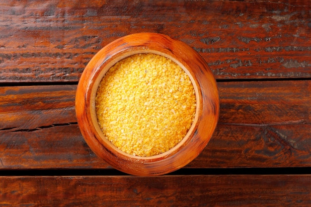 Raw cornmeal flour used in polenta in wooden bowl over rustic wooden table