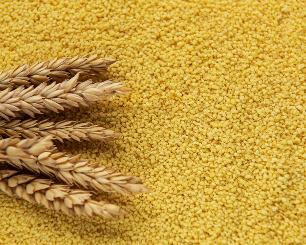 Raw Couscous and spikelets of wheat as a food background