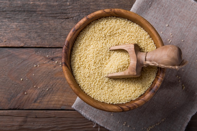 Raw couscous in a wooden bowl on the table