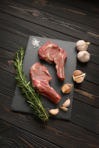 Raw cowboy steak and spices on a black wooden background