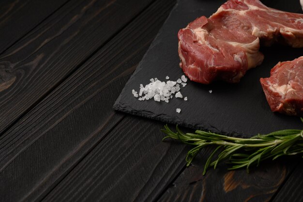 Raw cowboy steak and spices on a black wooden background