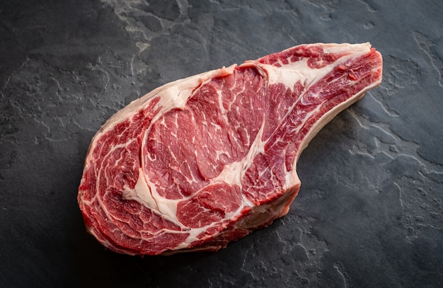 Raw cowboy steak on stone background, prime rib eye on bone, top view