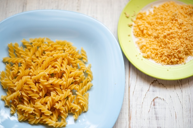 Raw curly pasta on a plate and grated cheese. Preparation for making pasta.