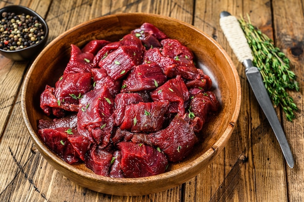 Raw cut wild venison meat for a goulash in a wooden plate. Wooden background. Top view.