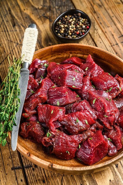 Raw cut wild venison meat for a goulash in a wooden plate. wooden table. Top view.