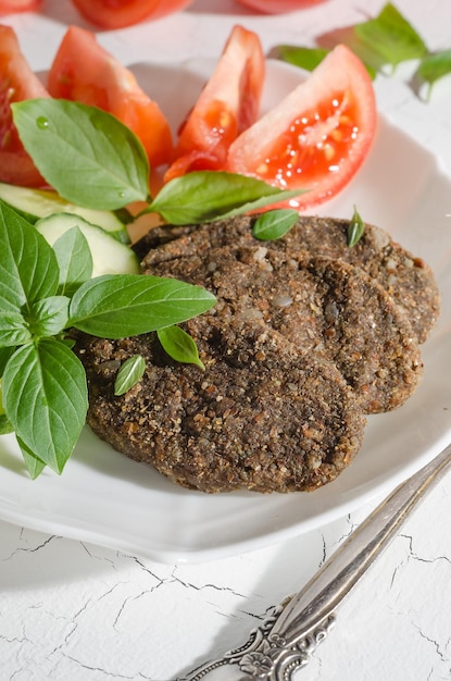Raw cutlet made from vegetables and cereals with vegetables and herbs on a white plate with hard light