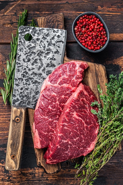 Raw denver cut black angus beef steak on a butcher board with
meat cleaver.