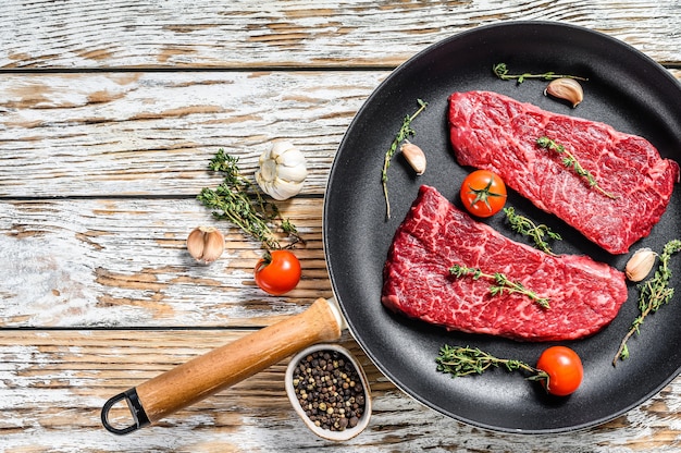 Raw Denver steak in a pan with herbs