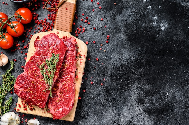 Raw Denver steak on a stone board with herbs