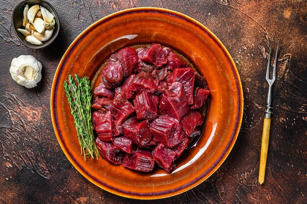 Raw diced deer steak for a venison goulash. Dark background. Top view.