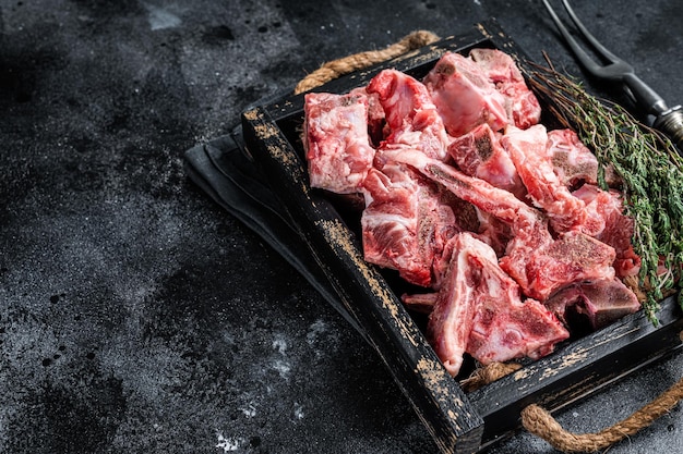 Raw diced meat with bone in a wooden tray. Black background. Top View. Copy space.