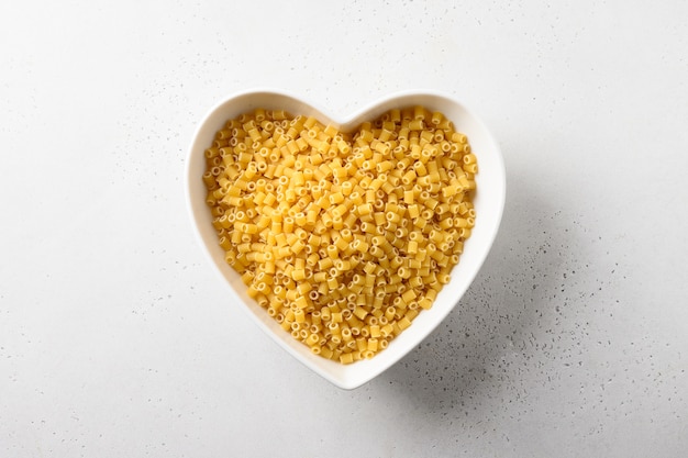 Raw ditalini pasta in white plate in shape of heart