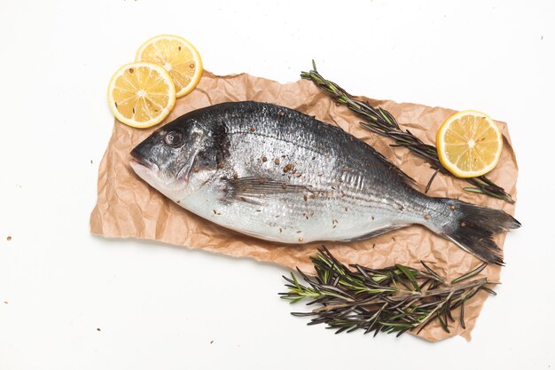 Raw dorada fish or gilthead bream on paper over white background, flat lay, top view