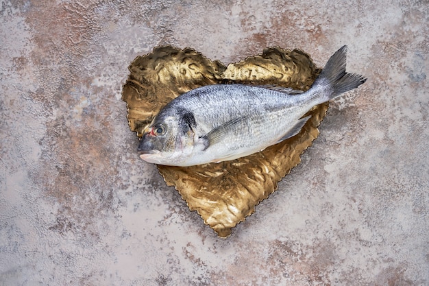 Foto pesce crudo di dorado sul piatto a forma di cuore. orata o pesce dorado. vista dall'alto, copyspace