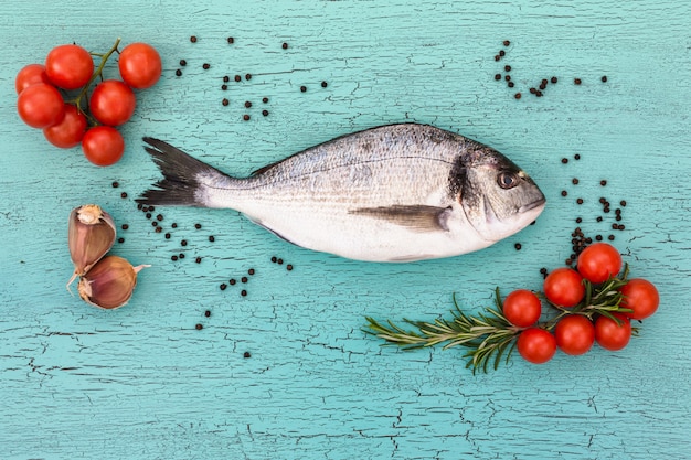 Raw dorado fish with cherry tomatoes on blue table. 