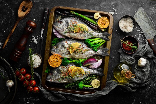 Raw Dorado fish with vegetables in a metal tray Fish cooking recipe Top view Free copy space On a black stone background