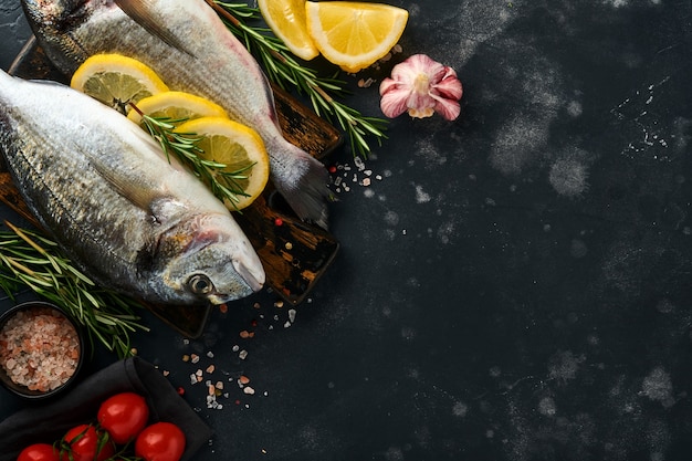 Raw dorado fresh fish or sea bream with ingredients for making\
lemon, thyme, garlic, cherry tomato and salt on a black slate,\
stone or concrete background. top view with copy space.