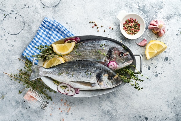 Raw dorado fresh fish or sea bream with ingredients for making lemon, thyme, garlic, cherry tomato and salt on light grey slate, stone or concrete background. Top view with copy space.