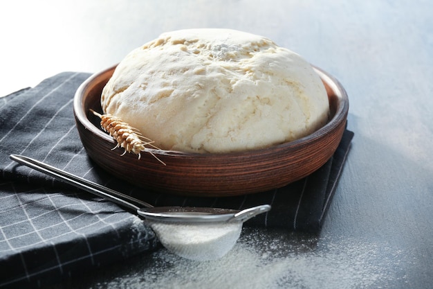 Raw dough in bowl and sieve with flour on grey table