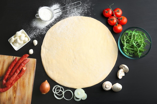 Photo raw dough for pizza with ingredients on kitchen table